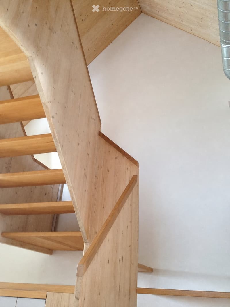 Modern wooden staircase with open risers and handrails, white walls, and a visible metal pipe on the right side.