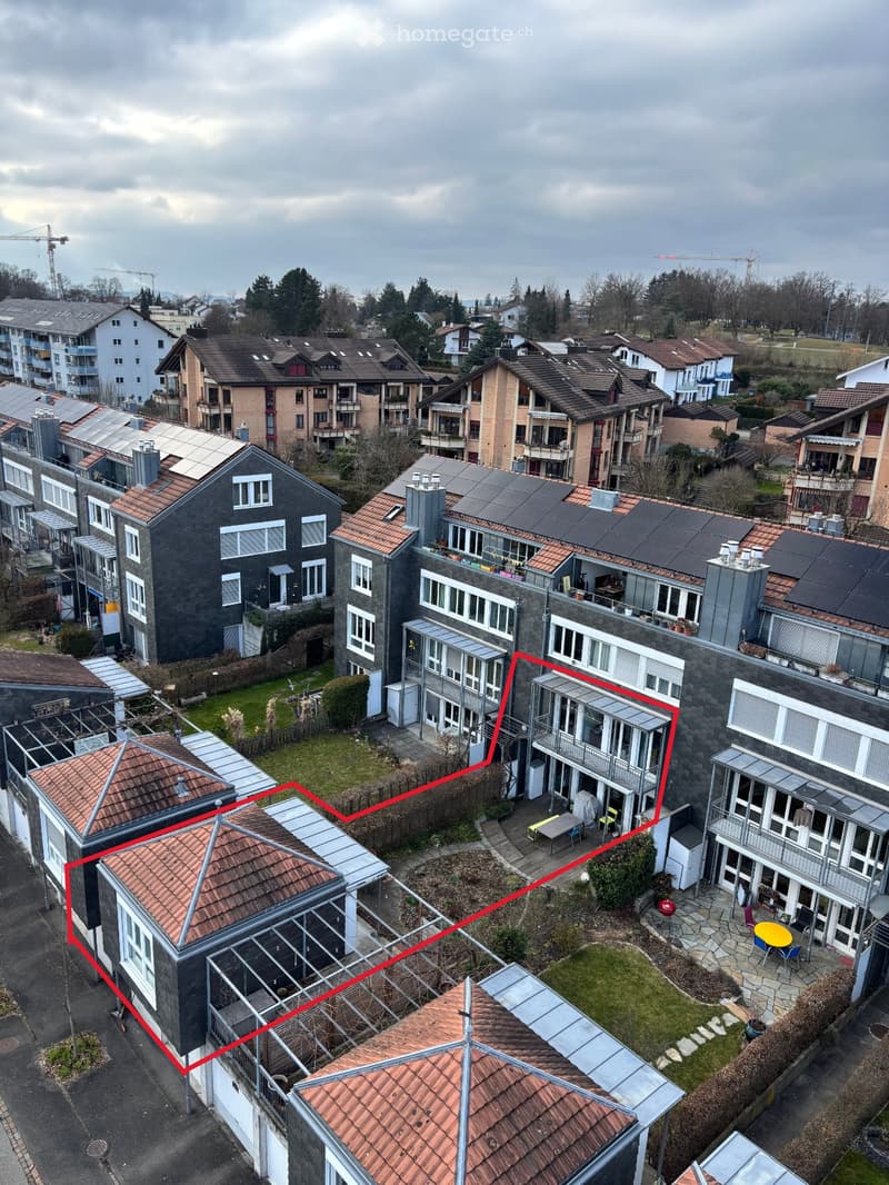 Aerial view of a residential area with multiple houses, solar panels on rooftops, and a fenced yard with outdoor furniture.
