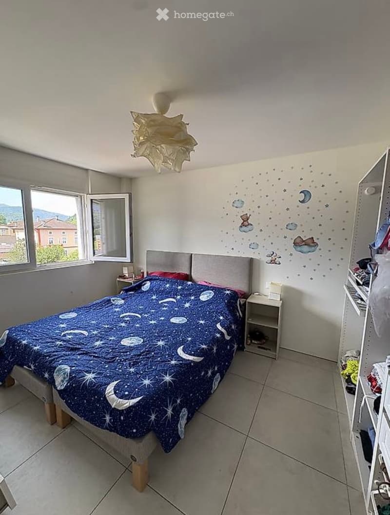 A child-friendly bedroom with a bed covered in a blue starry sky duvet, a nightstand, and a wardrobe. The walls feature a mural with clouds and stars.