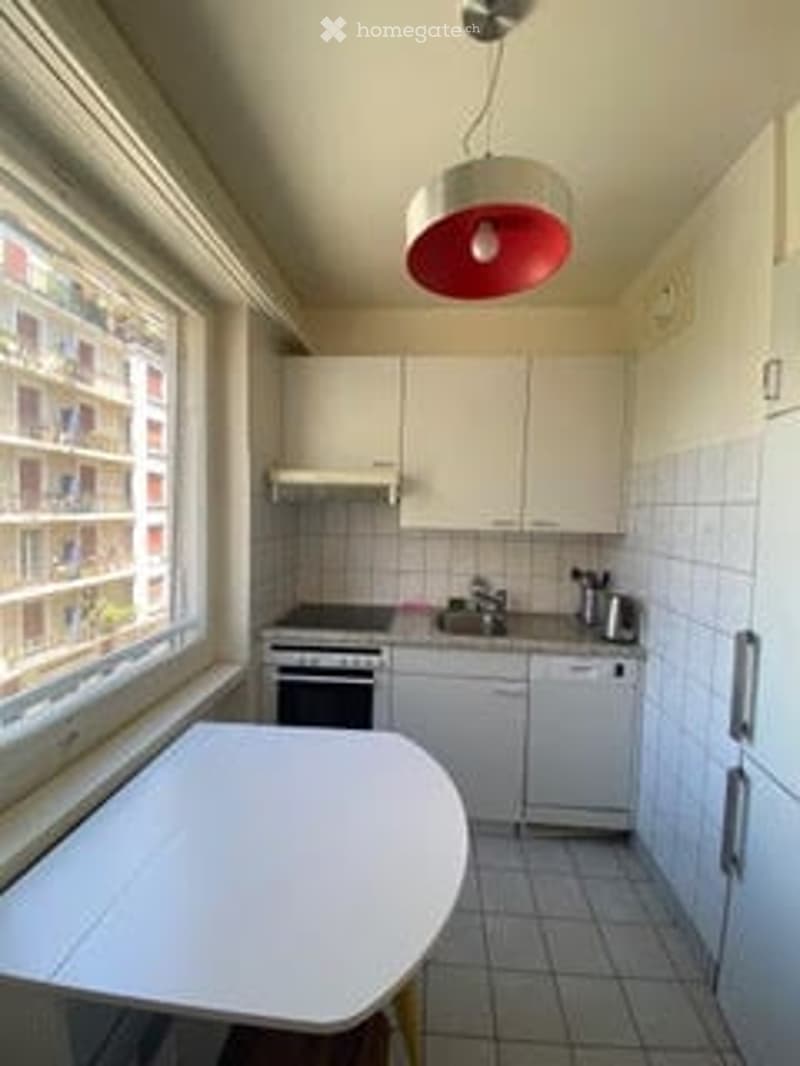 Modern kitchen with white cabinets, tiled floor, large window, and a round table.