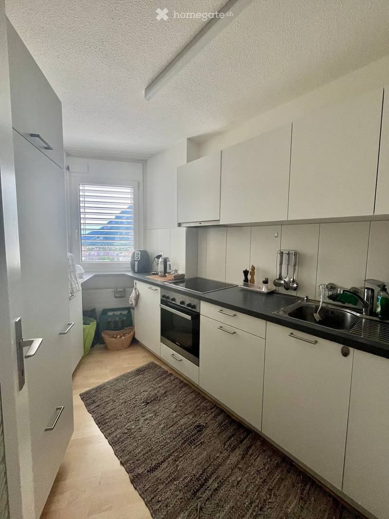 Modern kitchen with white cabinets, stainless steel appliances, and a black countertop. Features include an oven, sink, coffee maker, and various kitchen utensils.