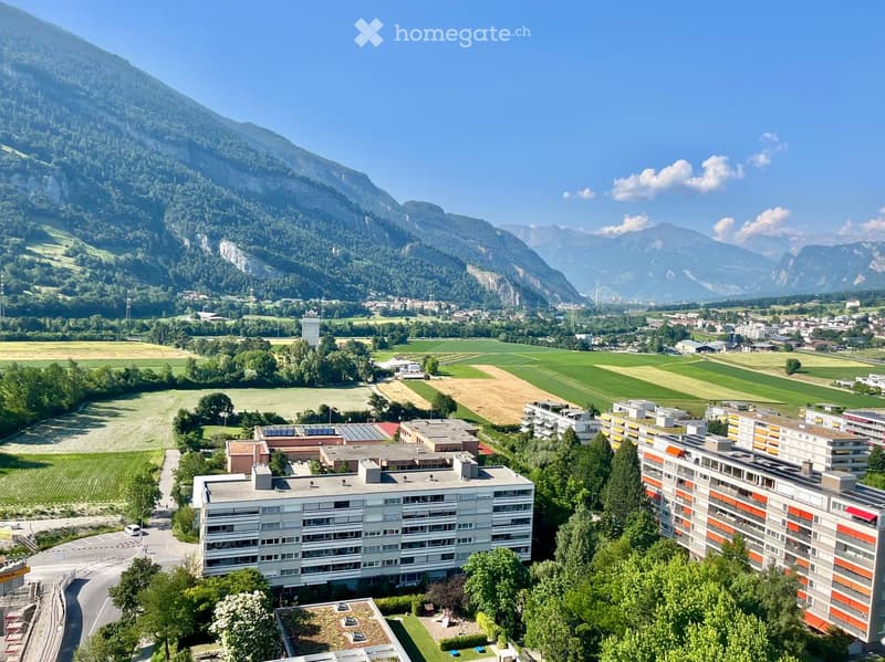 Aerial view of a residential complex surrounded by green fields and mountains in the background.