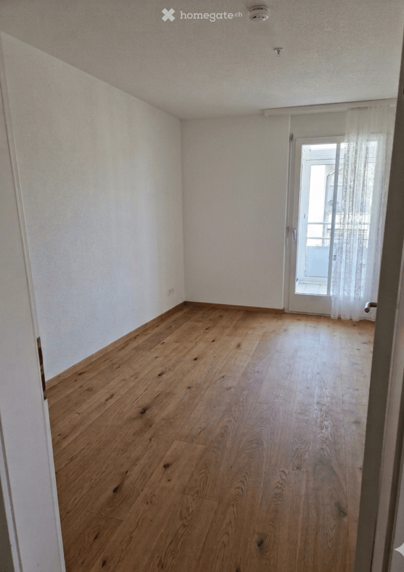 Empty room with wooden flooring, white walls, and a door leading to a balcony or terrace area.