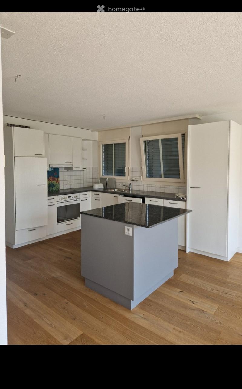 Modern kitchen with white cabinets, black countertops, central island, and wooden flooring.