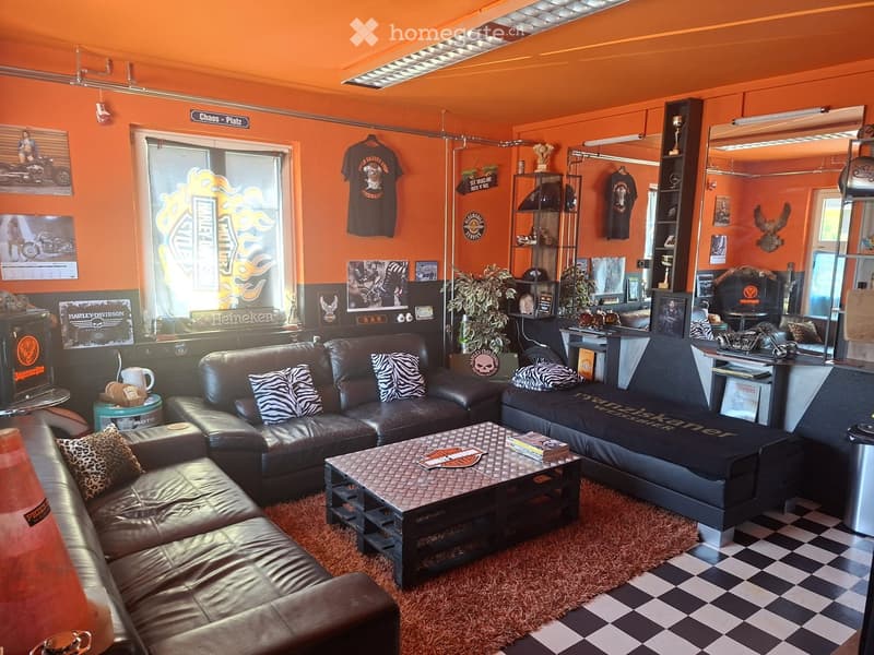 Vibrant orange-themed room with leather sofas, coffee table, large mirror, shelves with plants and memorabilia, and a checkered floor.