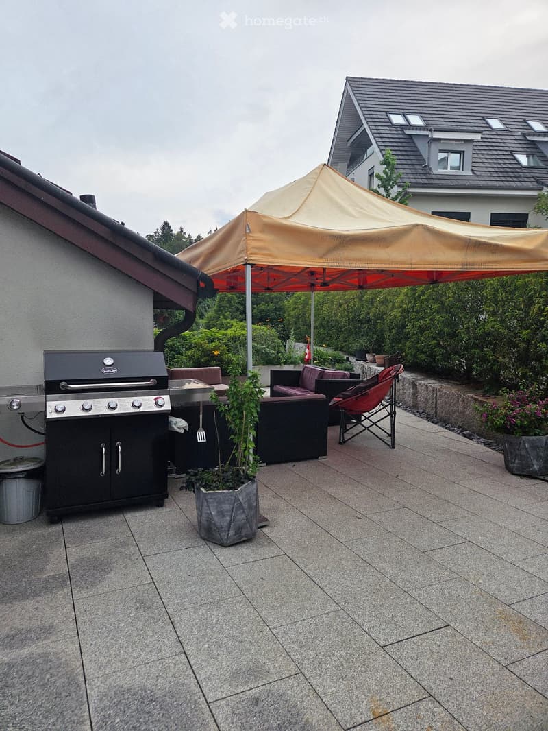 Outdoor patio with a grill, seating area, umbrella, and potted plants.