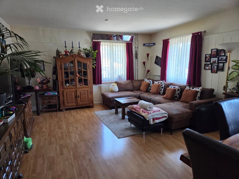 Living room with wooden flooring, large sectional sofa, coffee table, ottoman, cabinet, and decorative items.