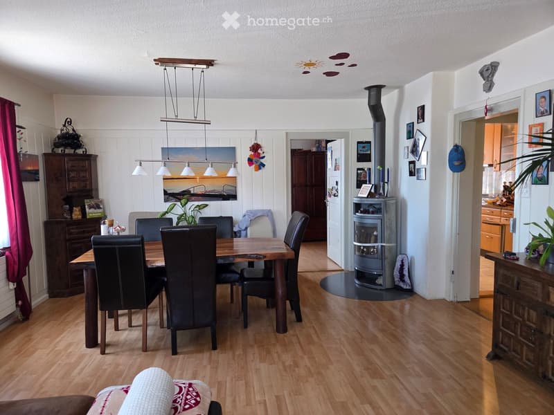 Dining area with a wooden dining table and black leather chairs, pendant lights, a wood stove, and a cabinet with decorative items.