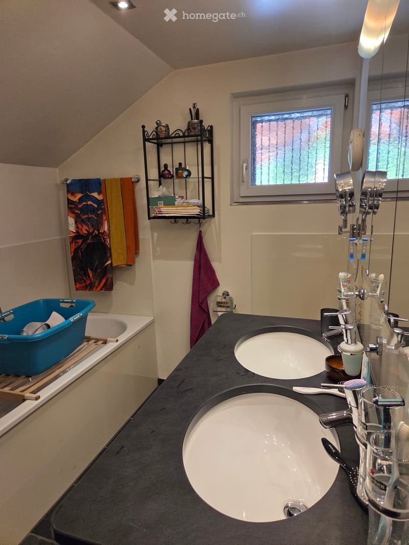 Modern bathroom with double sink vanity, bathtub, towel rack, and shelves holding toiletries and towels.
