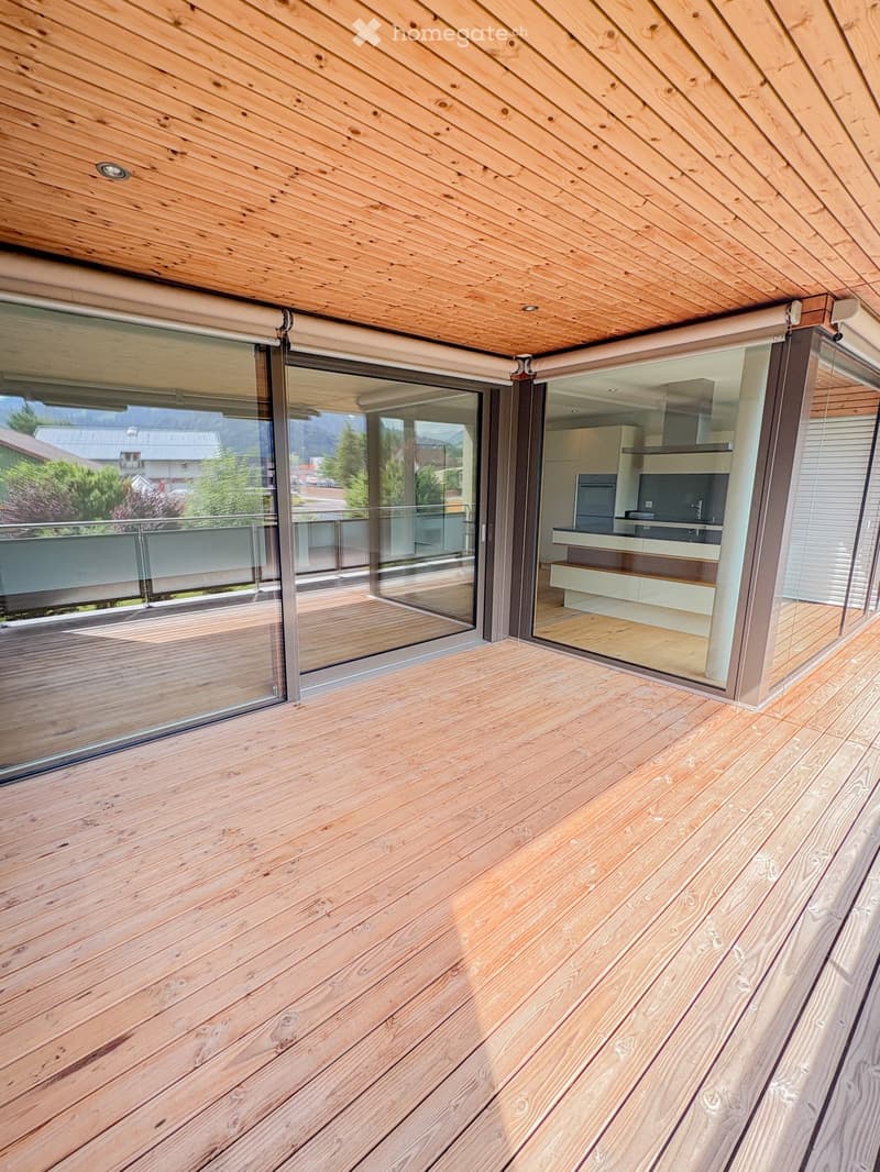 Wooden deck with large glass sliding doors leading to a modern kitchen, offering a scenic mountain view.