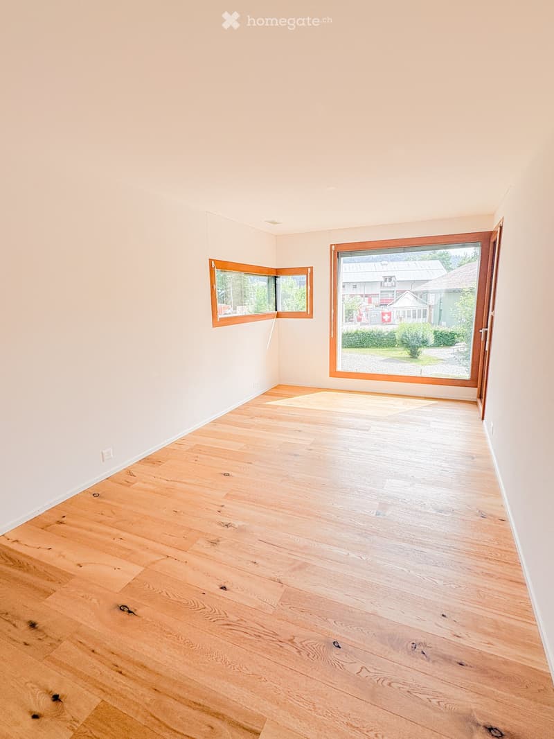 Empty room with light wooden flooring and white walls, featuring two windows and a door leading outside.