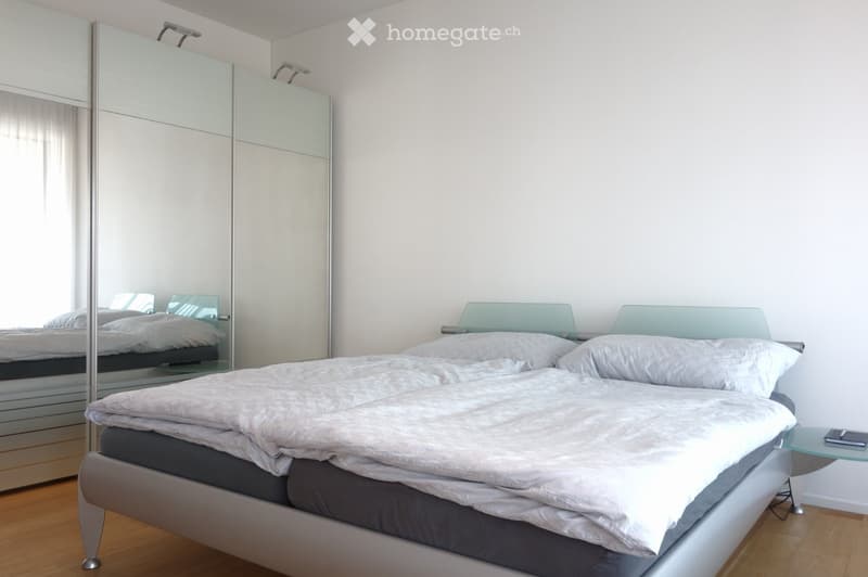 Modern bedroom with a large bed, mirrored wardrobe, and a small nightstand with a phone on it.