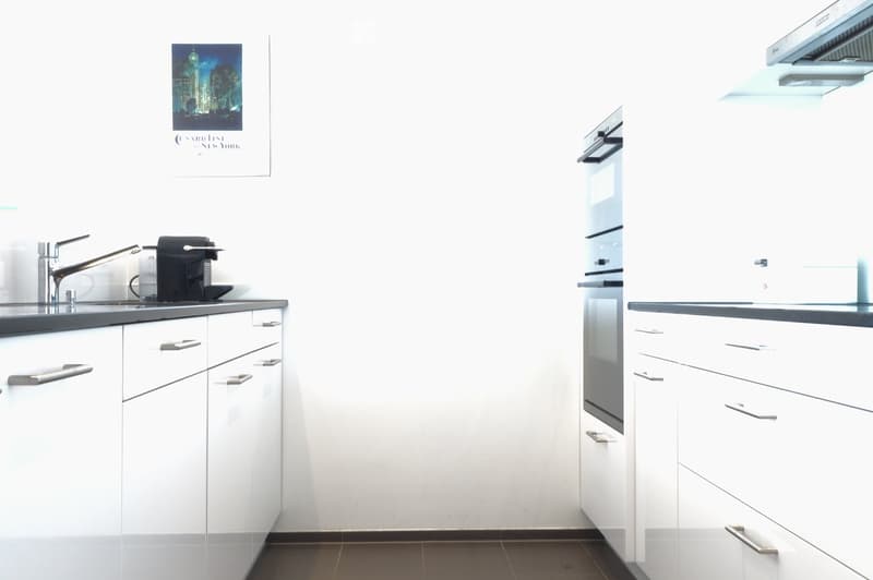 Modern kitchen with white cabinets, stainless steel sink, coffee maker, and built-in oven.