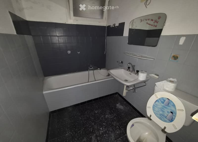 Bathroom with dark blue tiles on upper walls, grey tiles on lower walls, and black tiled floor. Includes a bathtub, sink, toilet, mirror, and faucet.