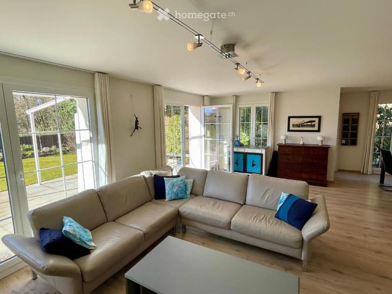 Modern living room with large windows, cream-colored sectional sofa, decorative pillows, coffee table, side table, and cabinet.