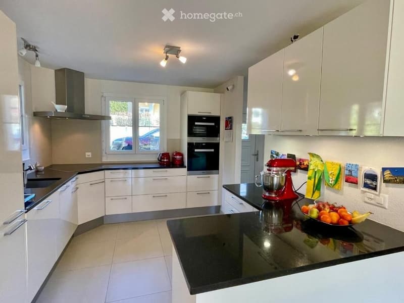 Modern kitchen with white cabinets, black countertops, stainless steel appliances, and a red stand mixer on the island.