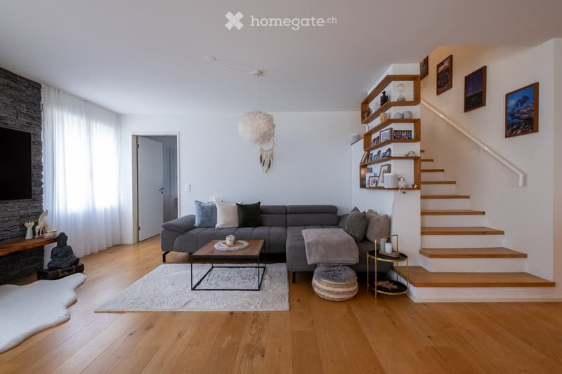 Modern living room with wooden flooring, grey sectional sofa, coffee table, floor lamp, and staircase leading to an upper level.