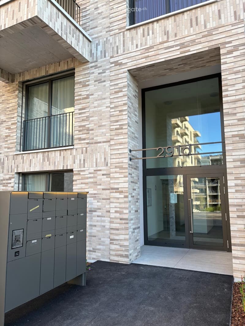 Modern building entrance with glass doors, brick facade, and mailboxes on the left side.
