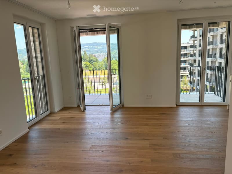Empty room with wooden flooring, large windows, and sliding glass doors leading to a balcony with a scenic view.