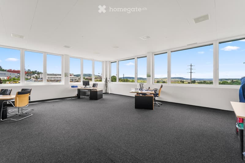Open-plan office space with large windows, desks, chairs, and computers.