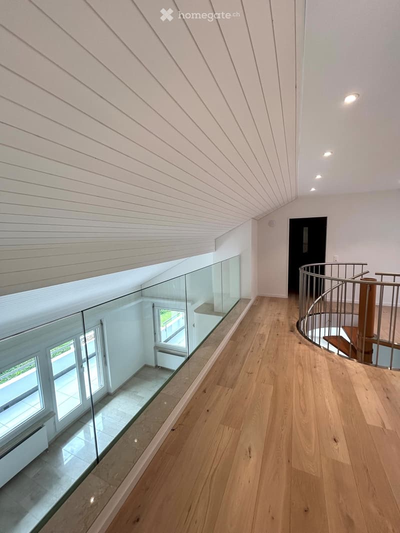 Modern hallway with wooden flooring, glass railing, and a spiral staircase leading upwards.