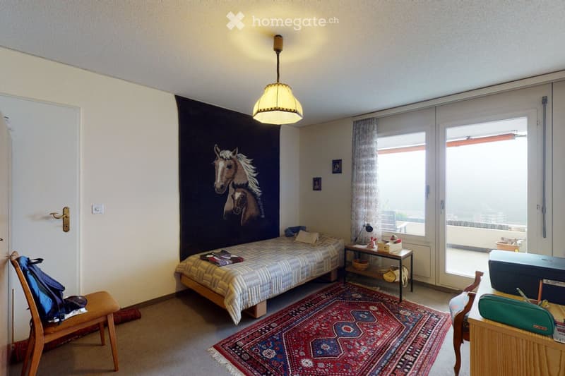 Cozy bedroom with a single bed, a patterned rug, a wooden chair, a small table, and a hanging lamp. A large mural of horses adorns one wall, and a sliding glass door leads to a balcony.