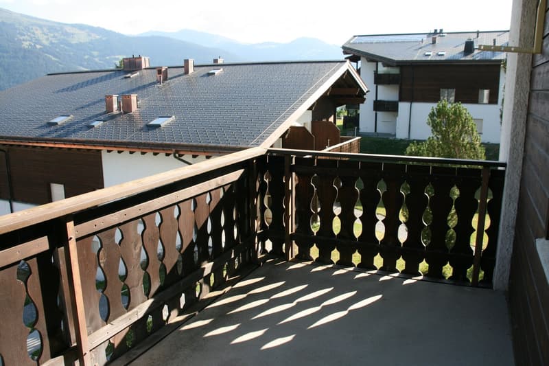 Balcony with wooden railing and decorative balusters, overlooking a scenic mountain view and neighboring houses.