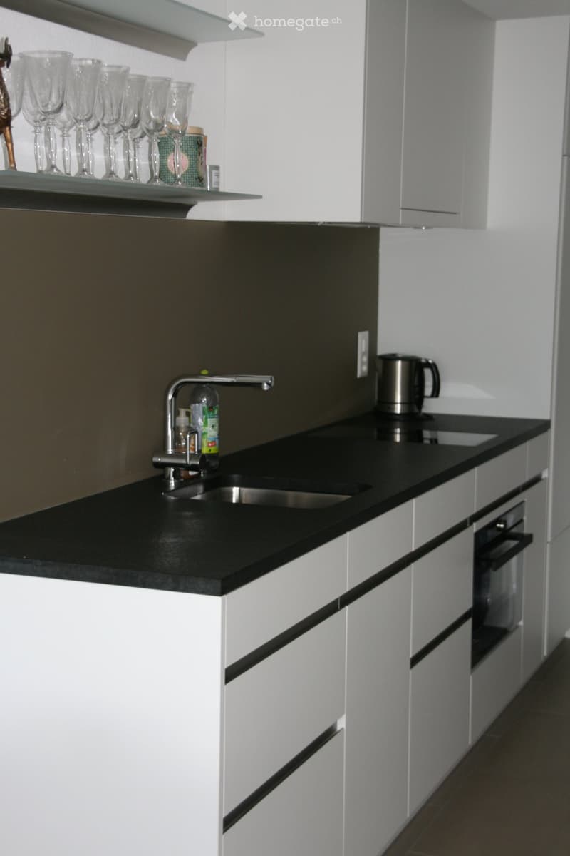 Modern kitchen with white cabinets, black countertops, and stainless steel sink and faucet. Shelves hold cups and decorative items.