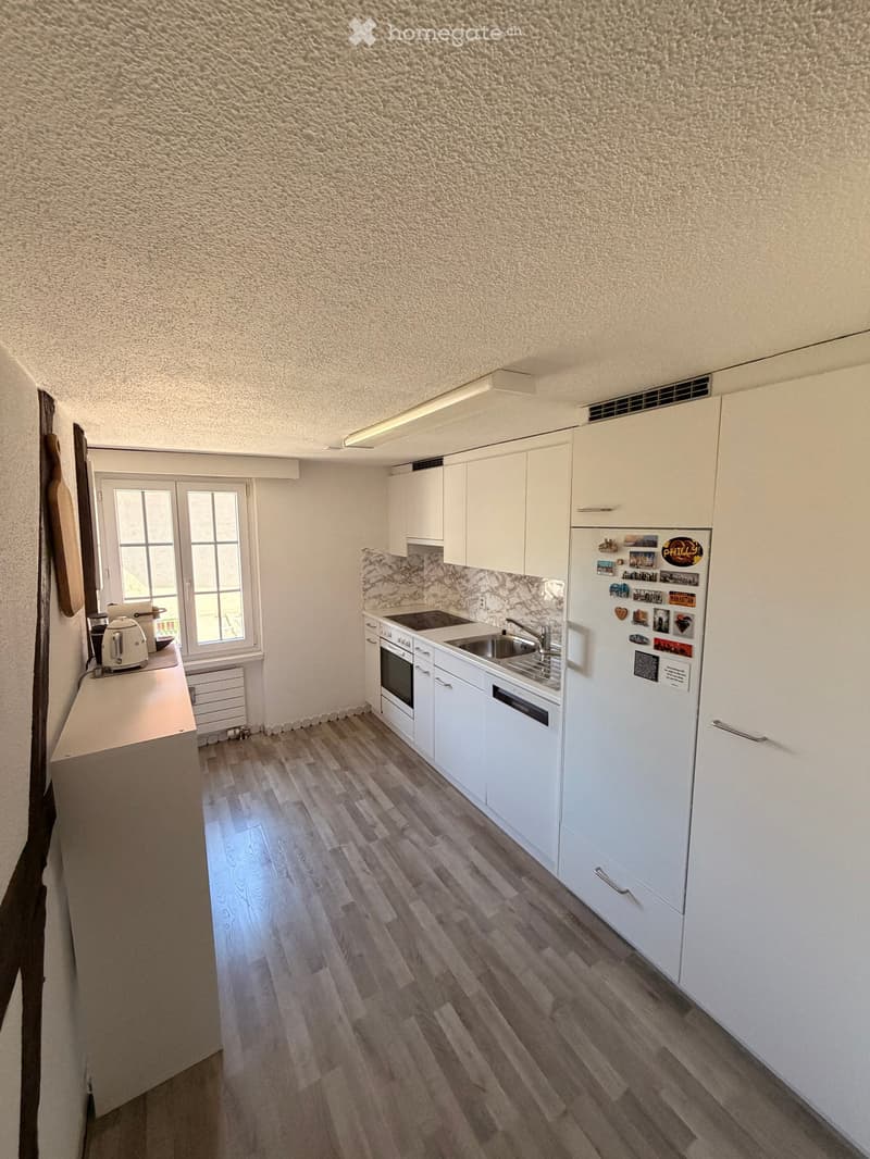 Modern kitchen with white cabinets, stainless steel appliances, wooden flooring, and a window.