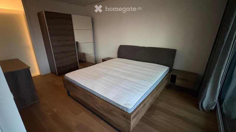 Modern bedroom with a wooden bed, white mattress, dark headboard, wardrobe, and nightstands.