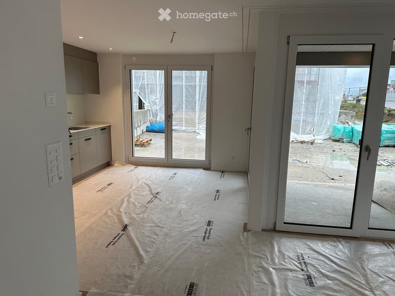 Empty room with bare walls, covered floor, and large glass doors leading to an outdoor area.