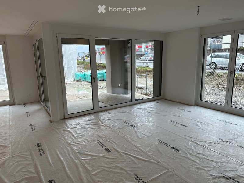 Empty room with white walls, large sliding glass doors, and protective plastic sheeting on the floor.