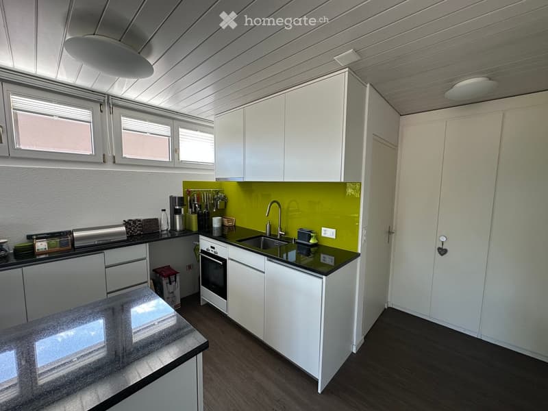 Modern kitchen with white cabinets, black countertops, stainless steel appliances, and a green backsplash.