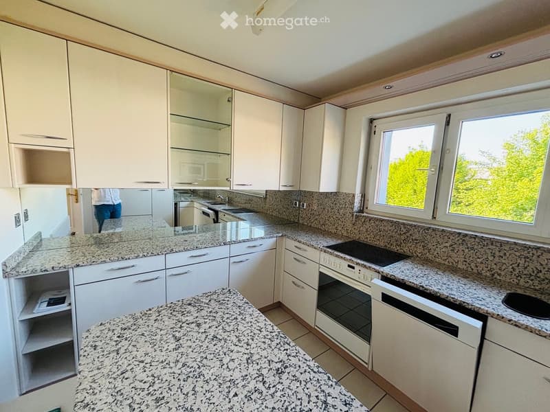 Modern kitchen with white cabinets, granite countertops, built-in oven, dishwasher, and sink.