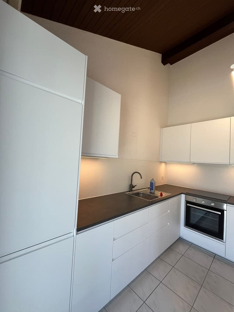 Modern kitchen with white cabinets, dark countertops, stainless steel sink, and oven. Features a bottle on the counter and a faucet above the sink.