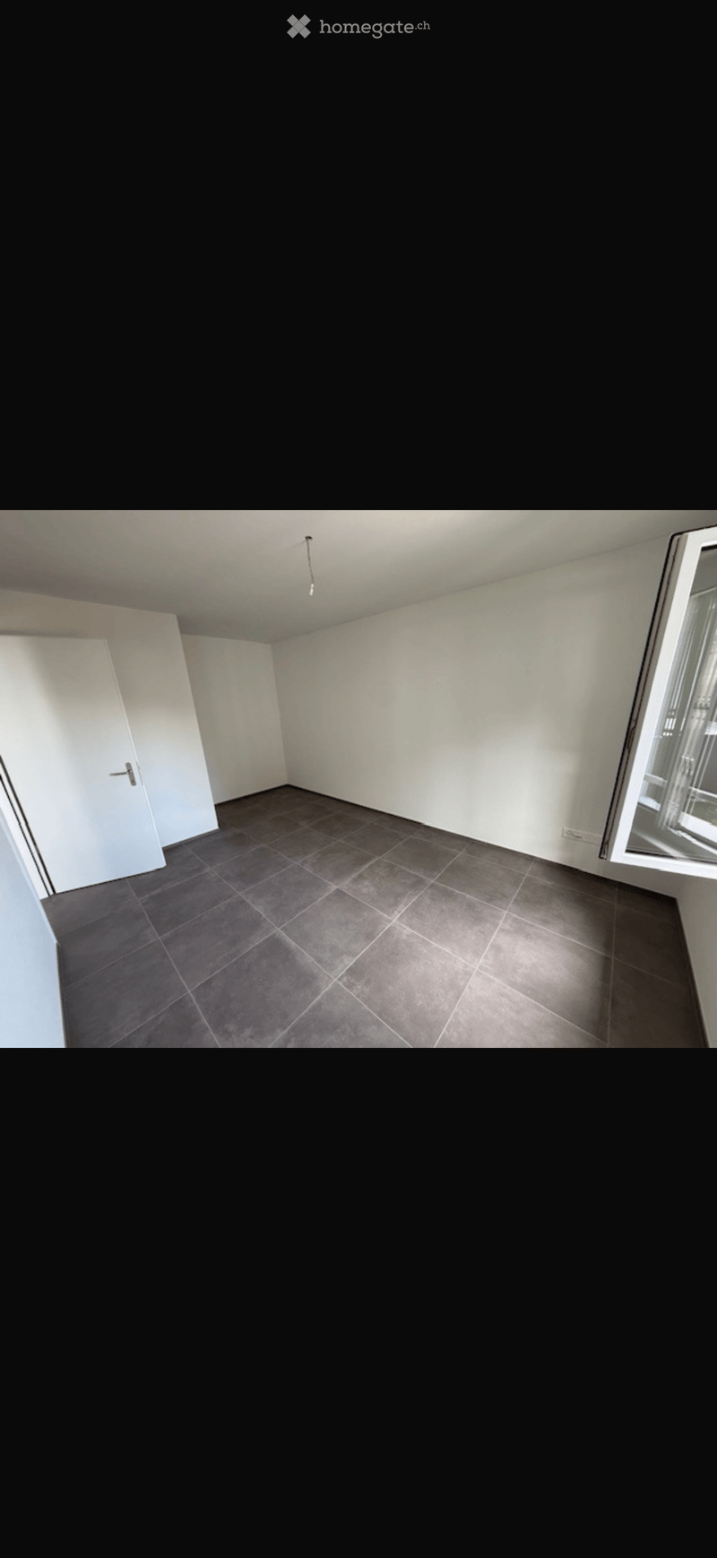 Empty room with grey tiled floor, white walls, and a single door. No furniture or equipment visible.