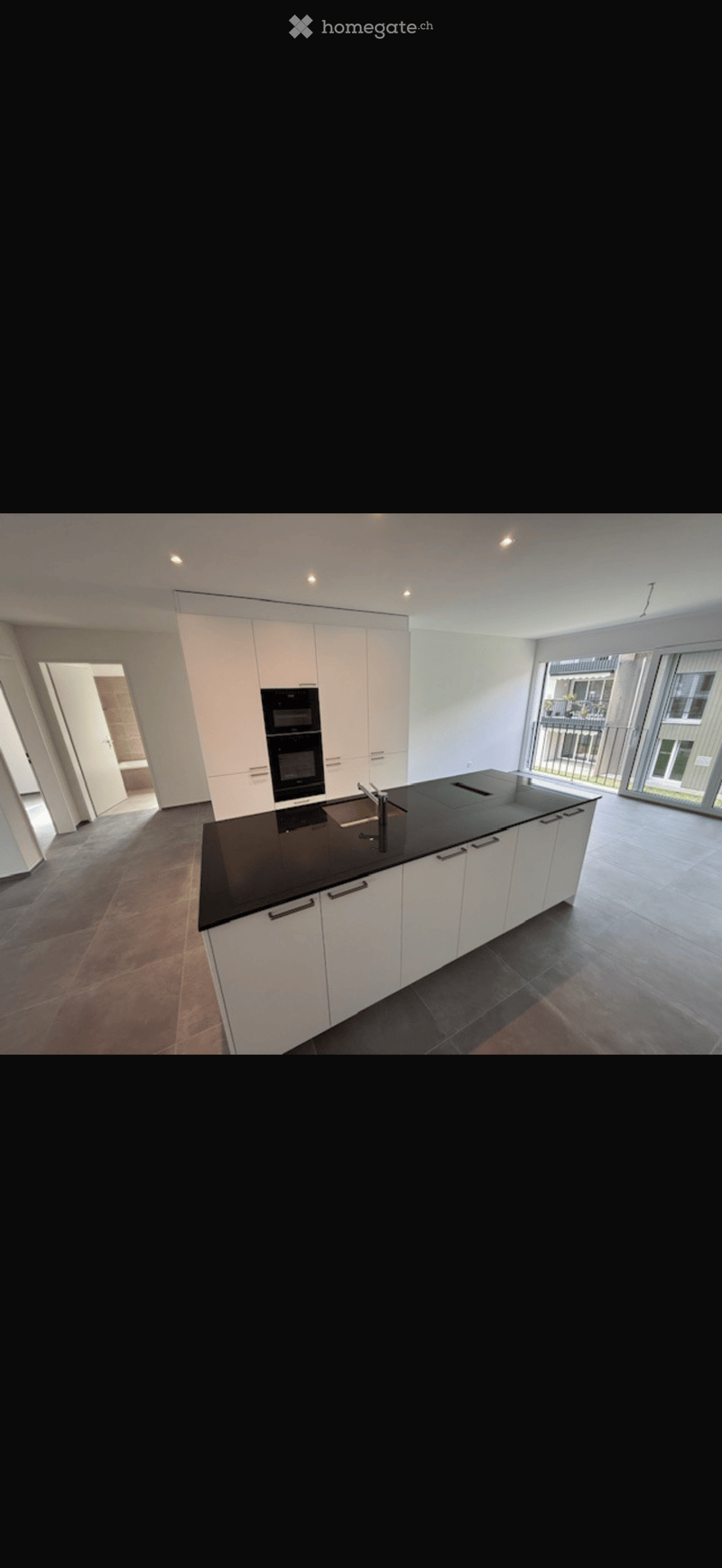 Modern kitchen with white cabinets, black countertop, stainless steel sink, and built-in oven.