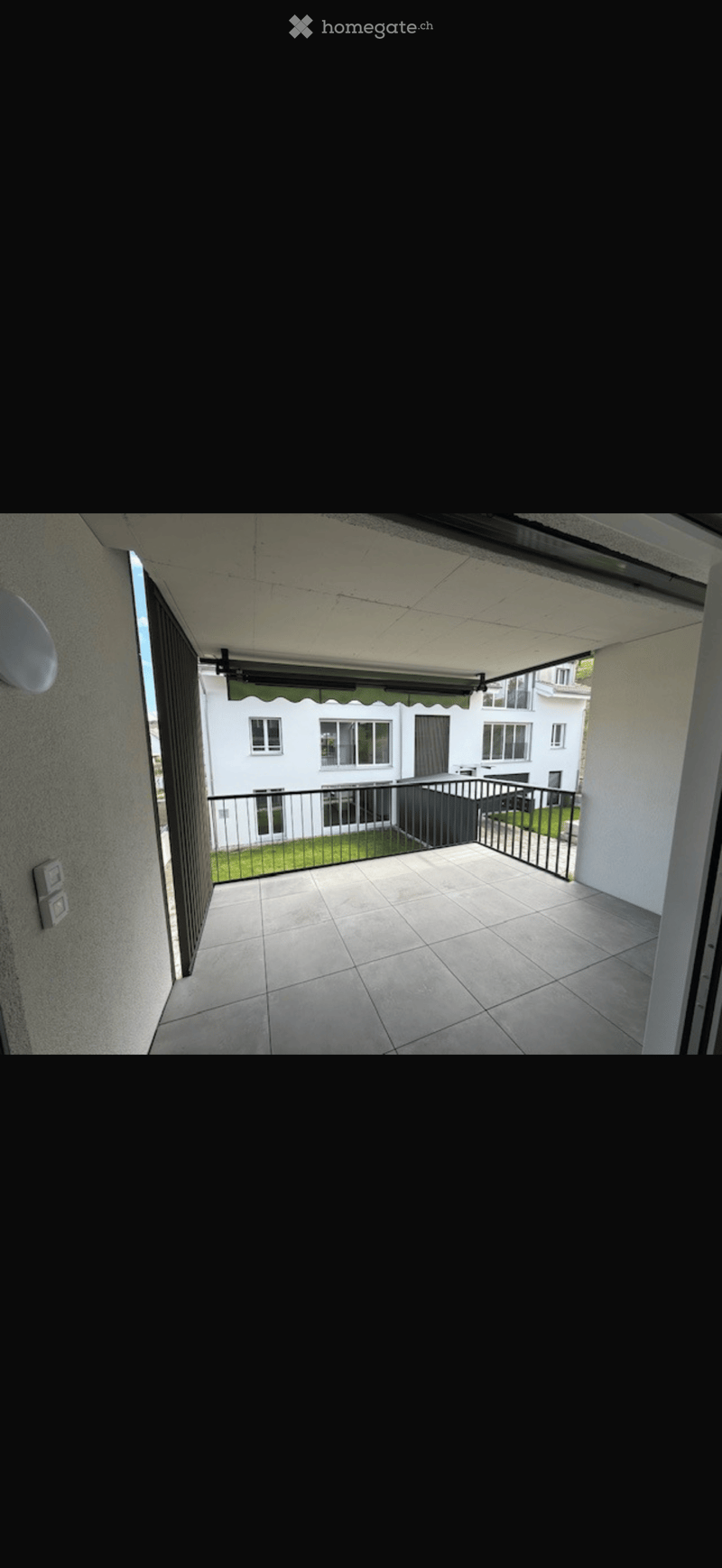 Balcony with tiled floor, metal railing, and a view of a neighboring building and small garden area.
