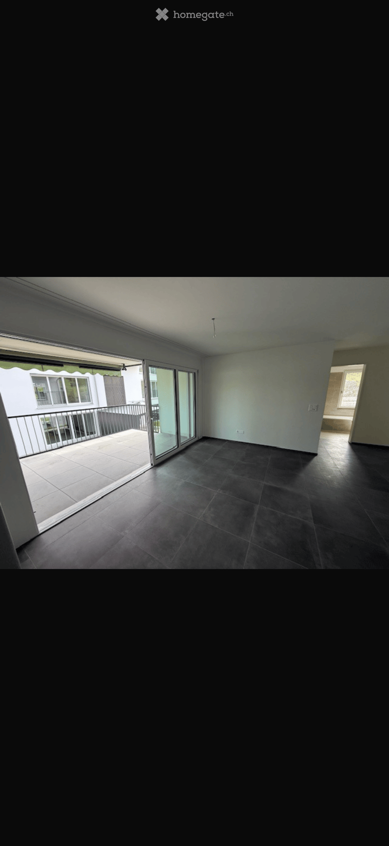 Empty room with dark tiled floor, white walls, and large sliding glass doors leading to a balcony.