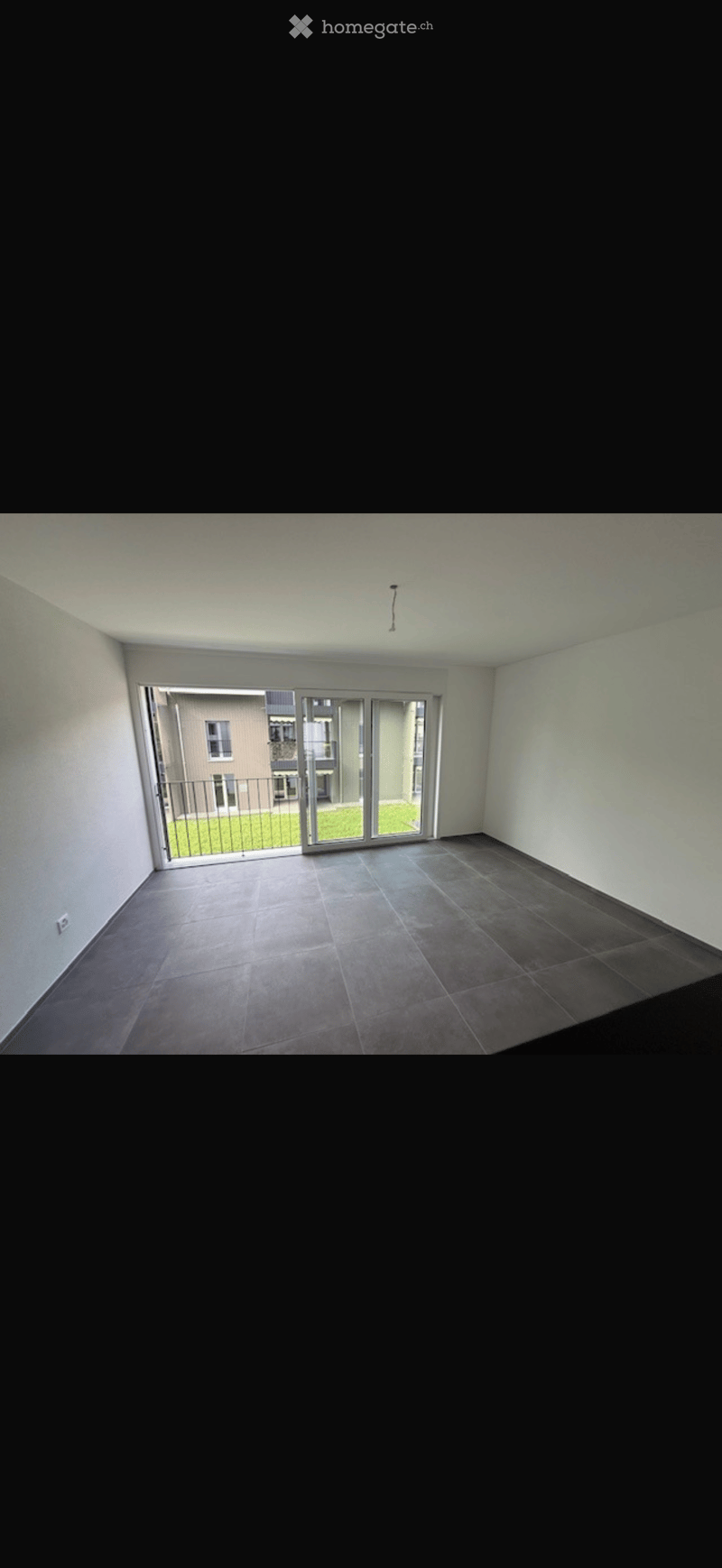 Empty room with tiled floor, white walls, and large sliding glass doors leading to a balcony or outdoor area.