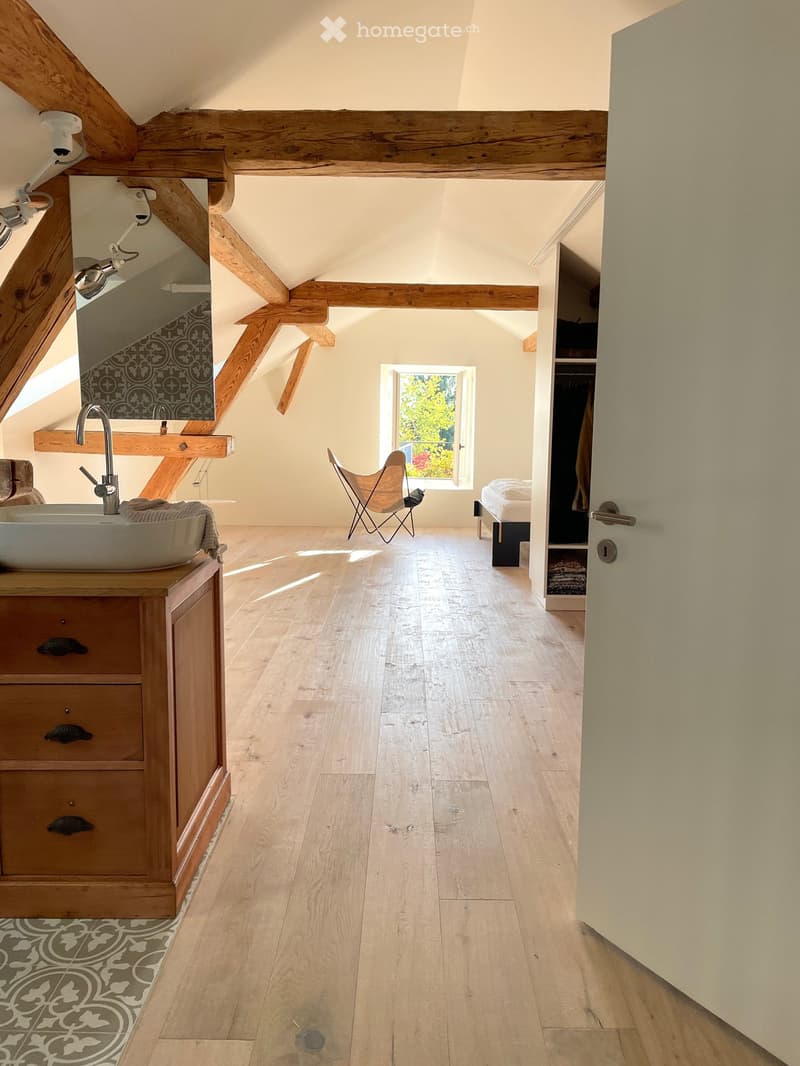 Bright, airy room with wooden beams, wooden floor, sink with faucet, chair, bed, and wardrobe.