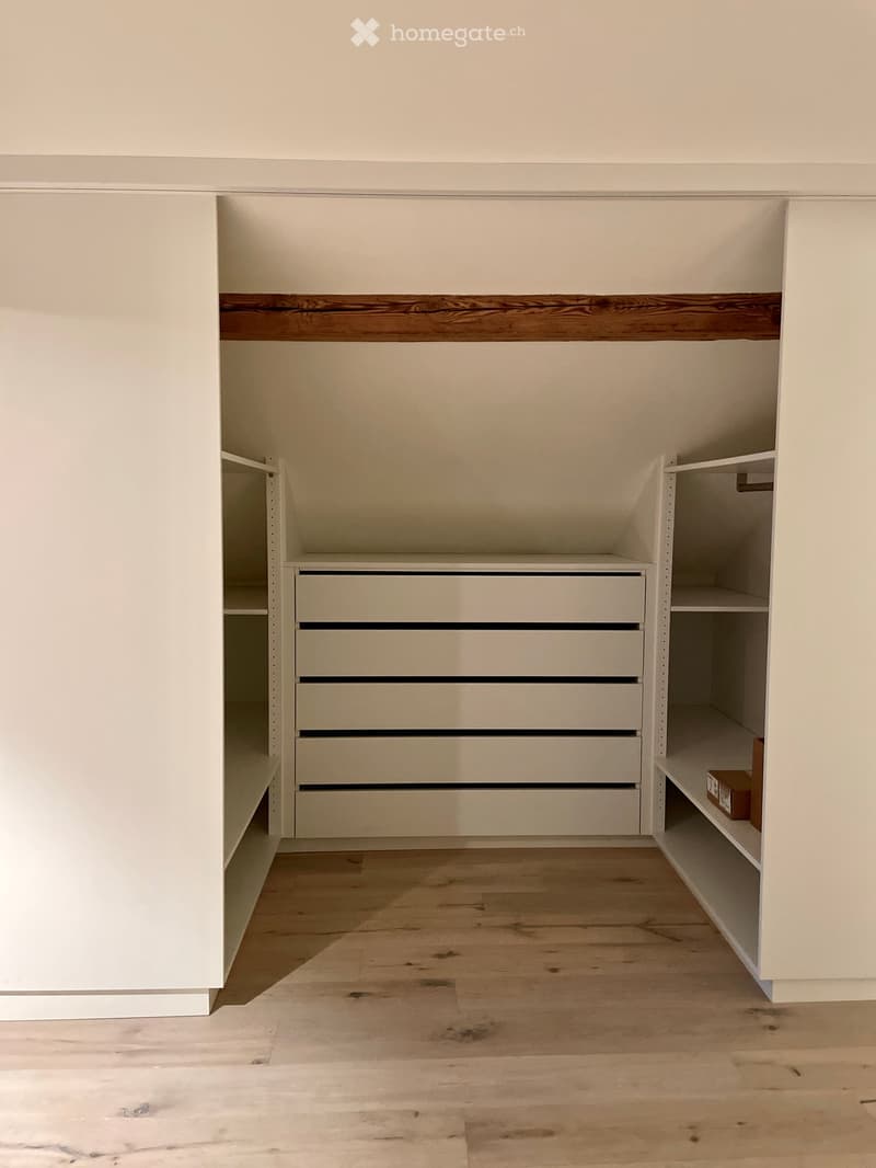 Empty room with light-colored wooden flooring, white walls, and built-in storage units including shelves and drawers.