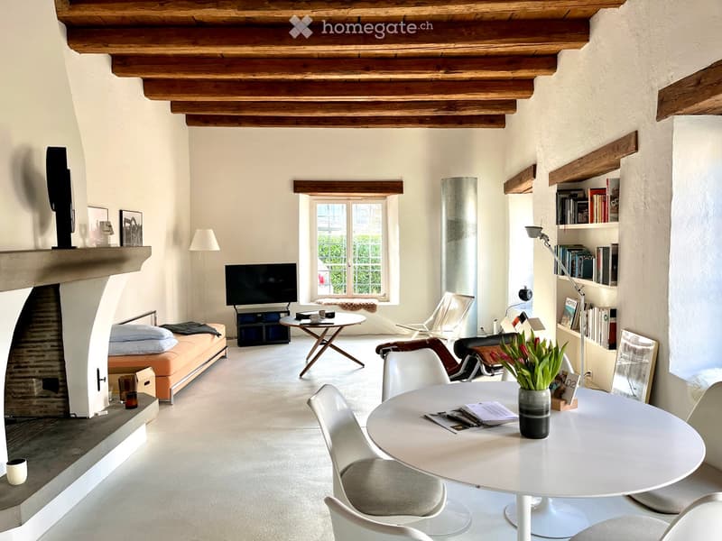 Living room with exposed wooden beams, fireplace, sofa, dining table, chairs, television, bookshelf, and floor lamp.