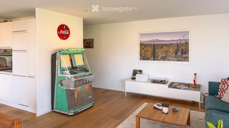 Living room with a green jukebox, a grey sofa, a wooden coffee table, a white cabinet, and a large picture frame on the wall.