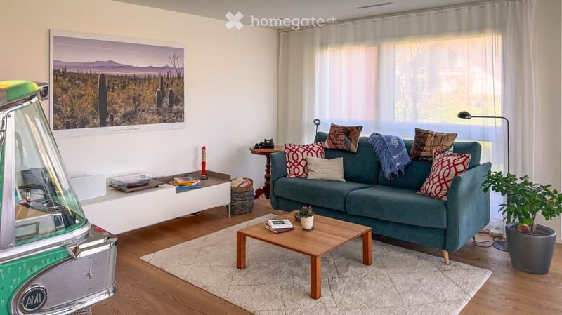 Modern living room with a green sofa, wooden coffee table, floor lamp, side table, potted plant, and a large picture frame on the wall.