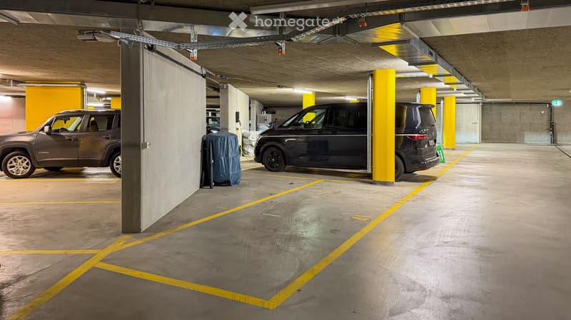 Underground parking area with several parked cars, yellow pillars, and marked parking spaces.