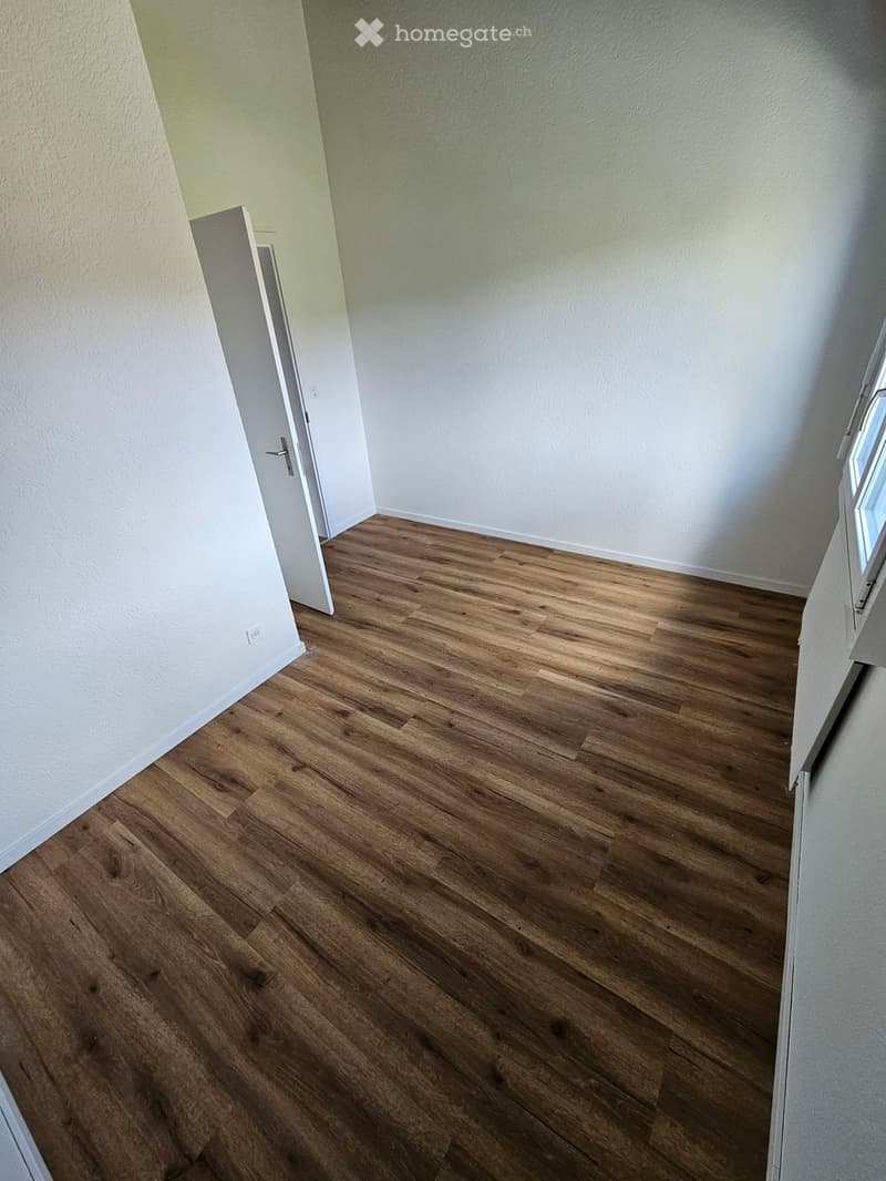 Empty room with wooden flooring and white walls, featuring a door and a window.
