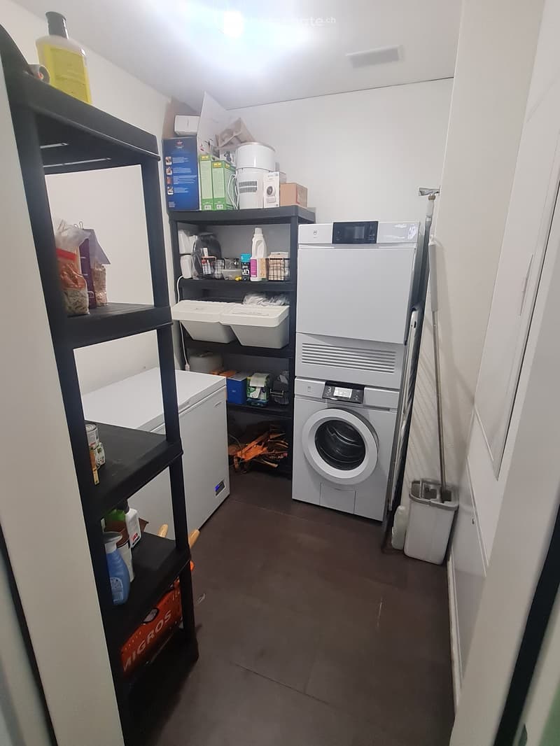 The image shows a utility room with a washing machine, dishwasher, and various storage shelves and containers. The room appears to be used for laundry and storage purposes.