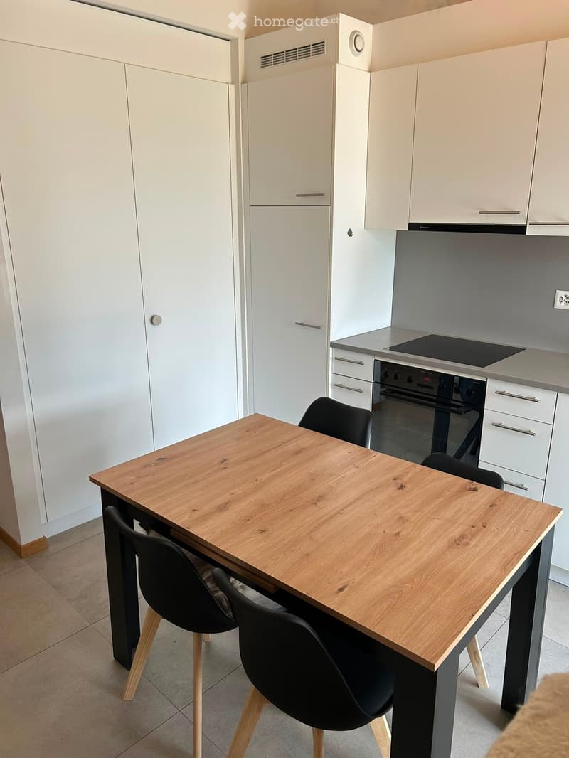 Modern kitchen with white cabinets, a wooden dining table, black chairs, and an oven.