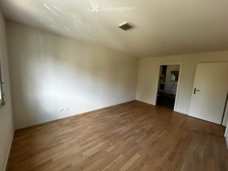 Empty room with wooden flooring and white walls, featuring a door leading to a bathroom.